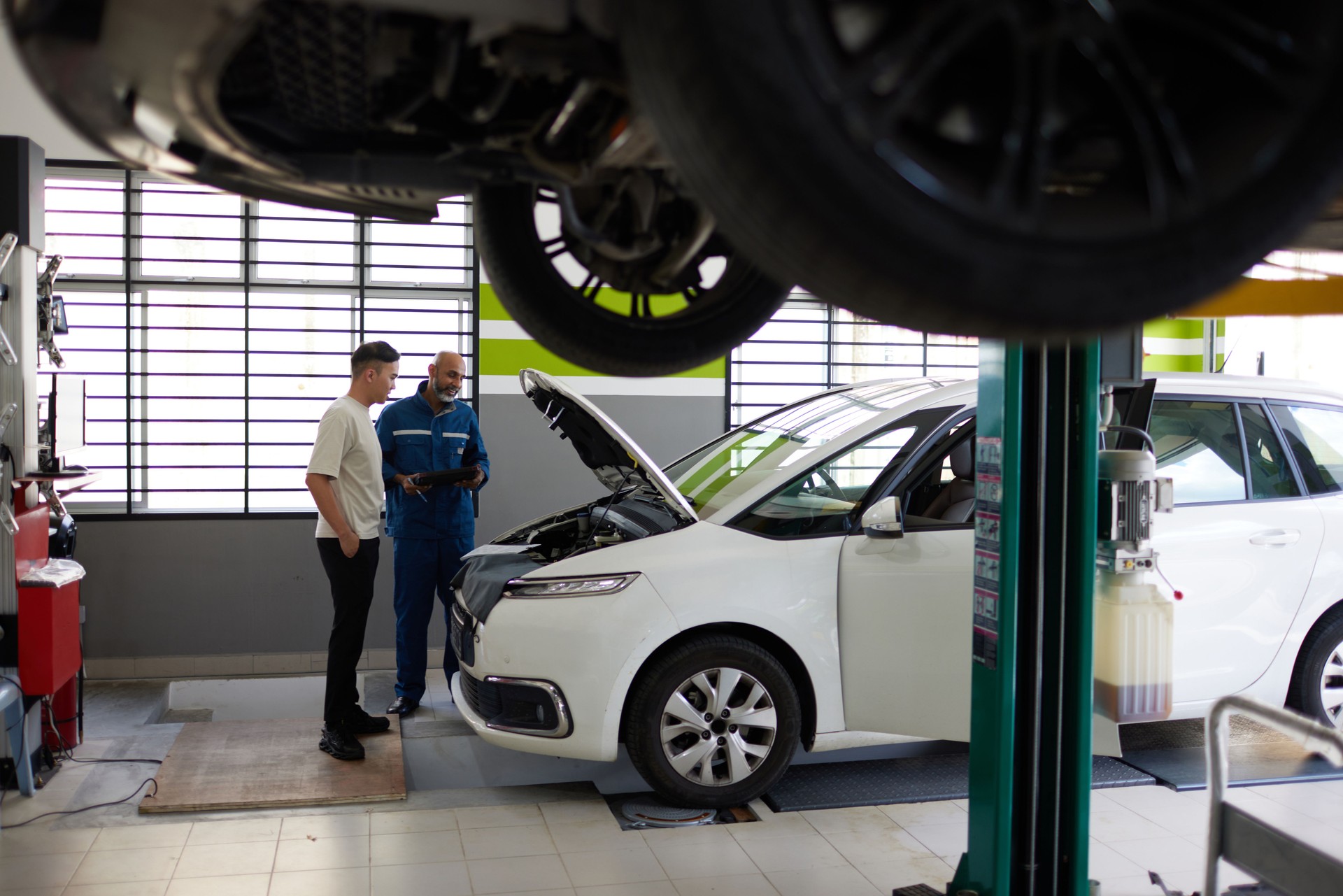 Asian car mechanic examines car bonnet with young asian male customer wide shot