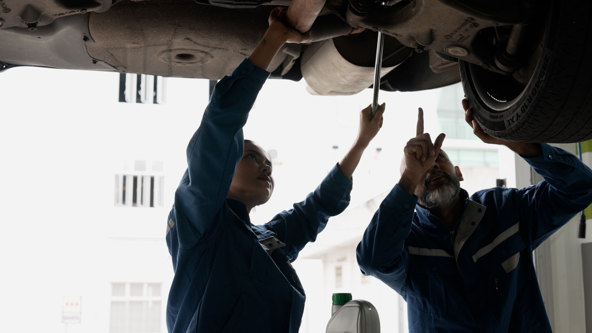 Female auto mechanic taking guidance from senior auto mechanic on vehicle servicing